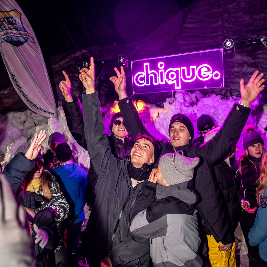 Feiernde Menschen vor dem pinken chique. Neonschild im Schnee